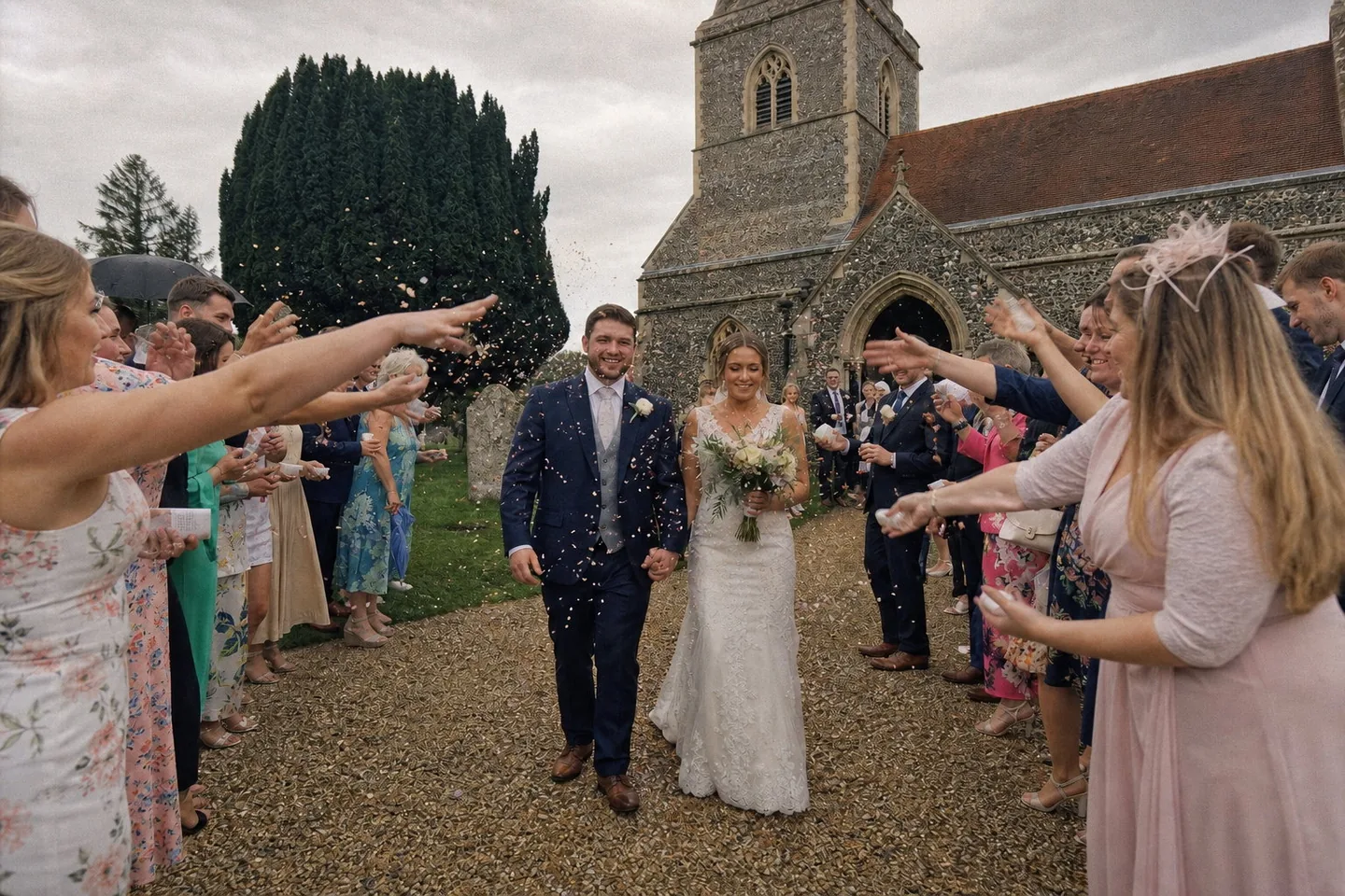 The same wedding photo on 35mm: the grey sky stays neutral, the dress stays white, skin turns gently warm, the greens go olive, and fine grain replaces the digital smoothness