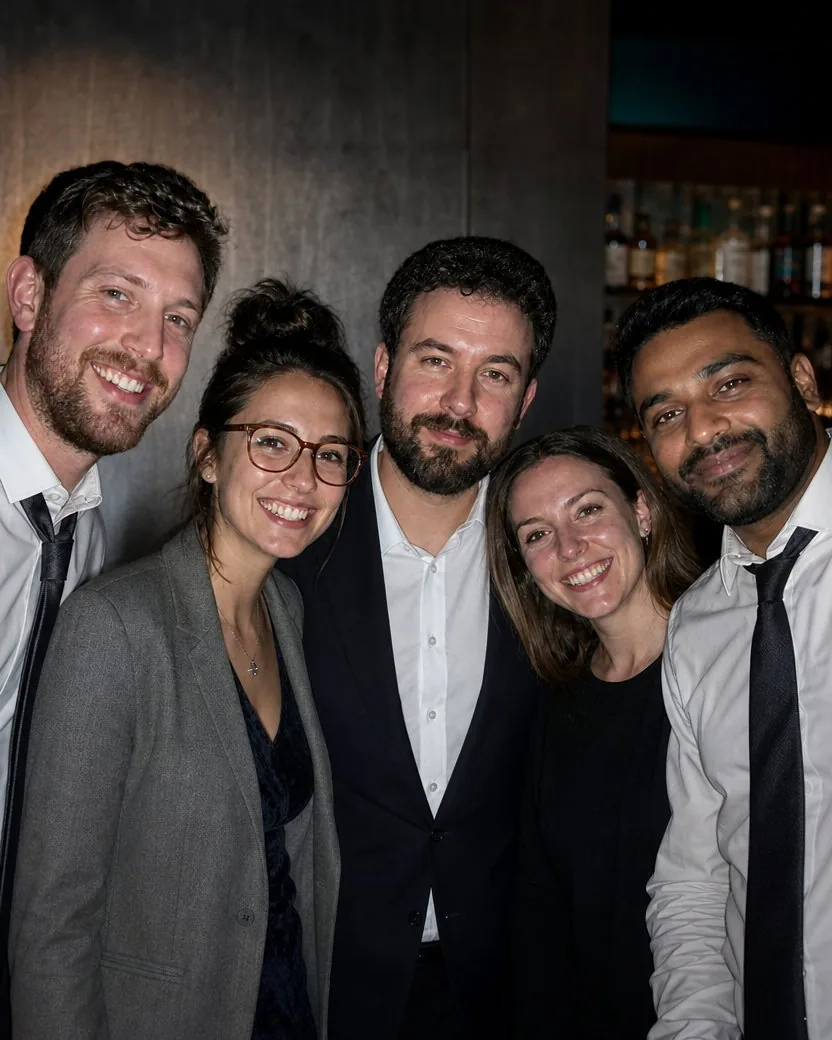 Portrait of the same five colleagues from the chest up in the same work clothes in the same bar, in two rows so every face is large and sharp, the drinks and the flash shadows gone