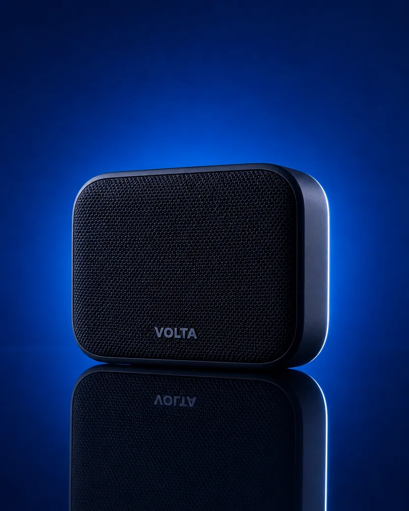 Ad photo of the same black speaker with the “VOLTA” wordmark on a deep electric blue set, a hard rim light down its right edge and the speaker mirrored in the glossy floor below