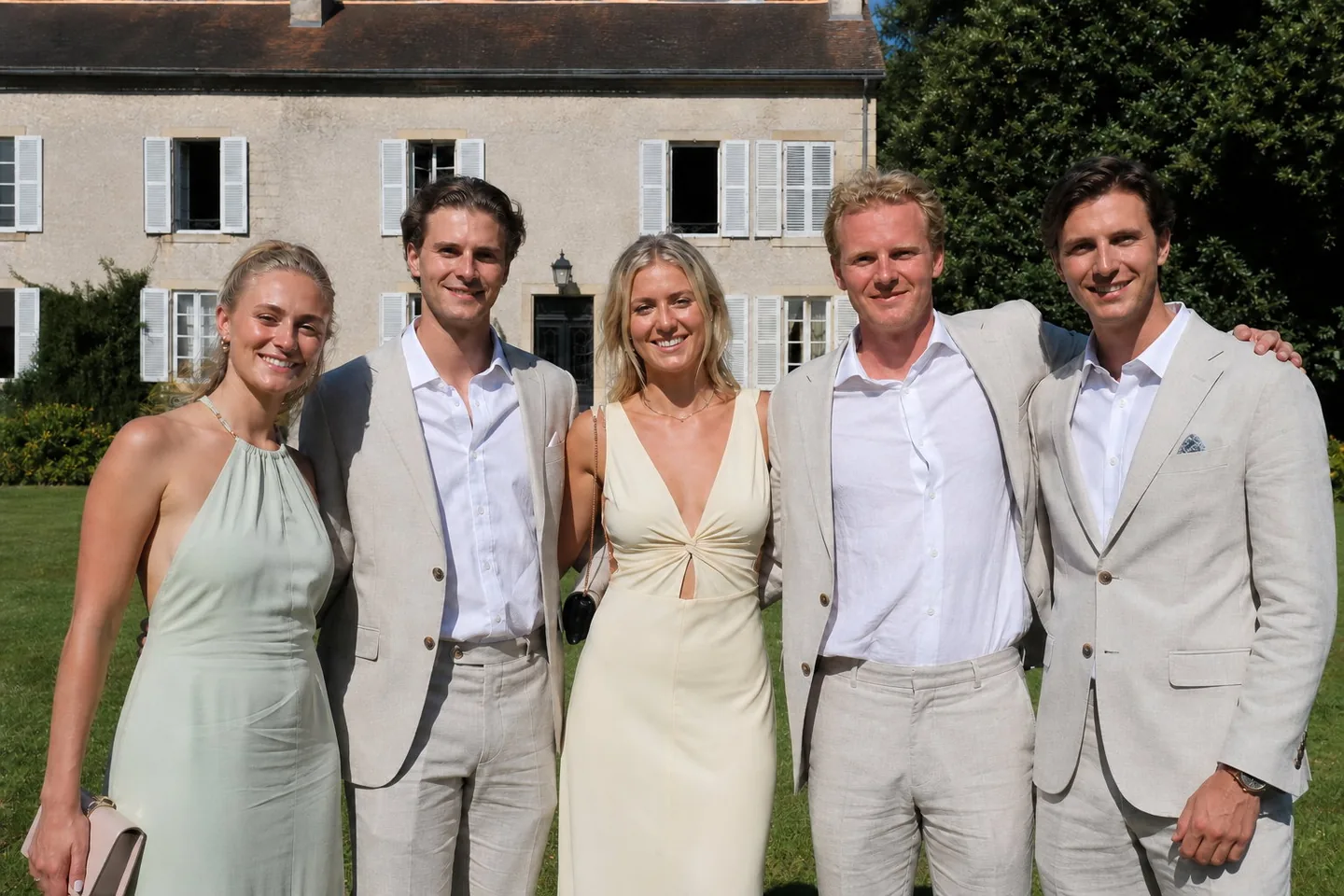 The same wedding group photo with the shine and the flushed face calmed, the flyaway hair tidied, and the harsh shadows softened on all five guests evenly