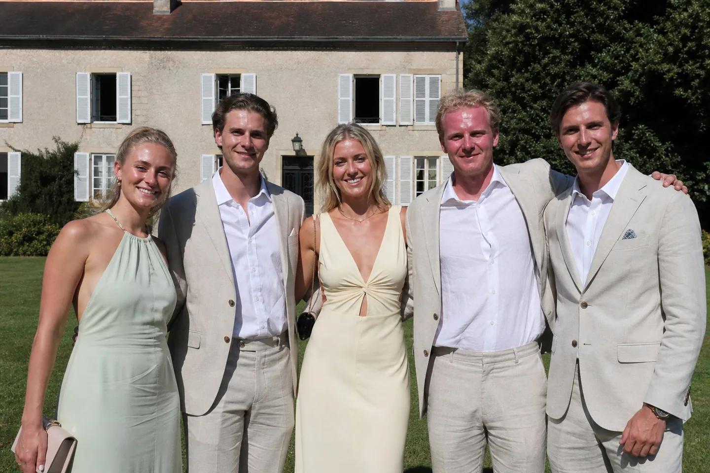 Phone photo of five wedding guests in summer formal clothes squinting in harsh midday sun with shiny foreheads, one flushed red face, and flyaway hair